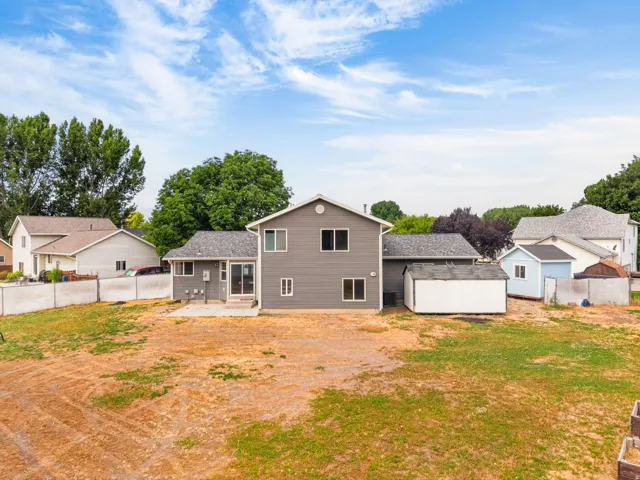 Expansive rear yard featuring a concrete patio, two outbuildings, and a perimeter chain-link fence
