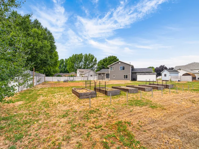 Expansive backyard featuring multiple raised garden beds, a partial privacy fence, and mature perimeter trees