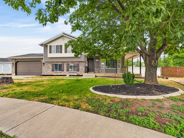 Split-level residence featuring a two-car garage, stone and siding exterior, and a covered porch entry