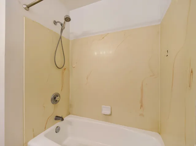 White bathtub with a chrome showerhead and faucet, set against cream-colored shower surround panels