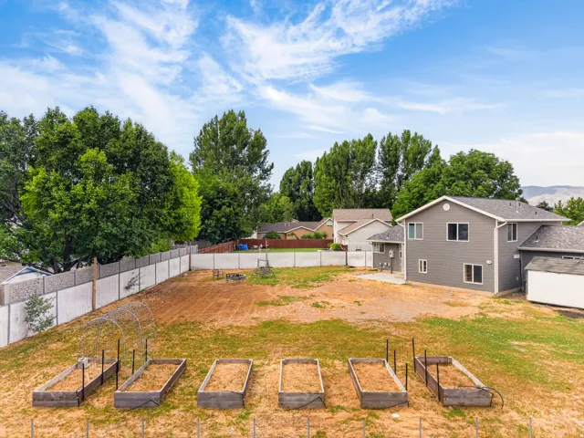 Expansive property featuring multiple raised garden beds, a dedicated planting area, mature perimeter trees, and a concrete patio