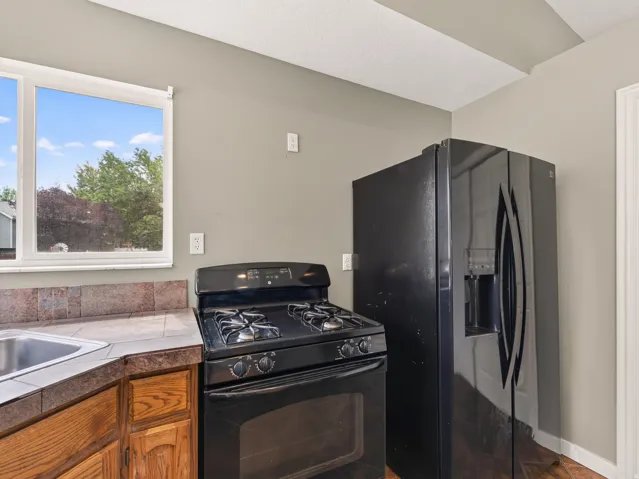 Kitchen featuring a black gas range, black side-by-side refrigerator with exterior dispenser, tile countertops, and a stainless steel sink