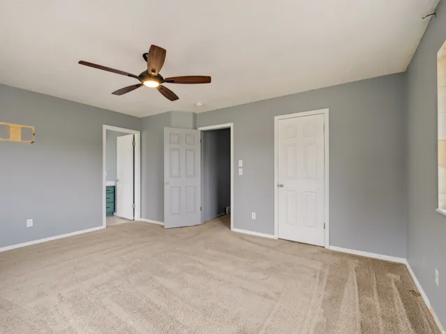 Carpeted room featuring light gray walls, a ceiling fan with wood-finish blades, and white interior doors