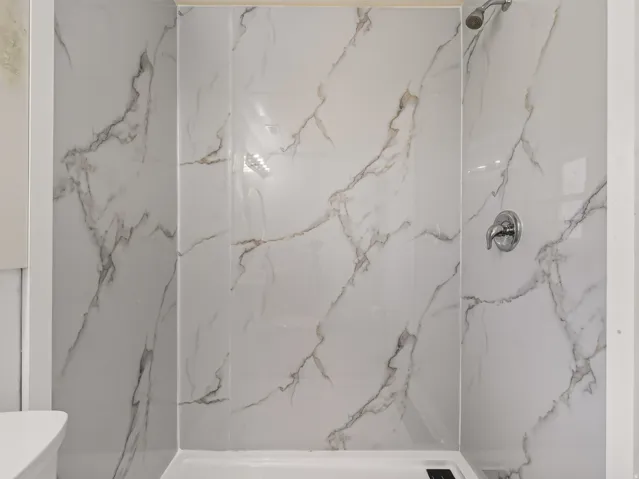 Shower enclosure featuring white marble-look wall tiles with grey veining, a chrome showerhead, and a chrome single-handle shower valve