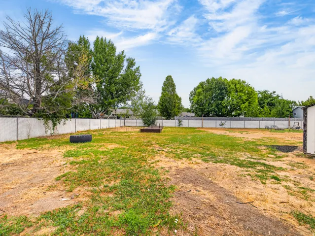 Expansive backyard featuring a partial chain-link fence, mature trees, and a visible outbuilding