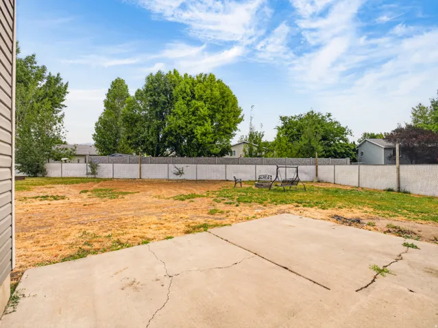 Expansive backyard area featuring a concrete patio, perimeter fencing, and mature trees