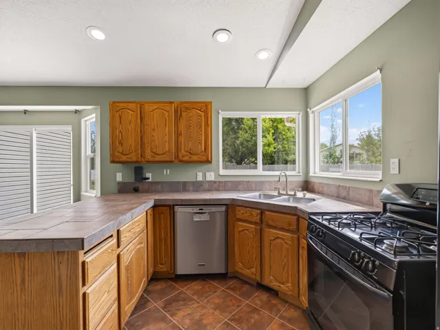 Kitchen featuring oak cabinetry, tile countertops, stainless steel dishwasher, and a gas range