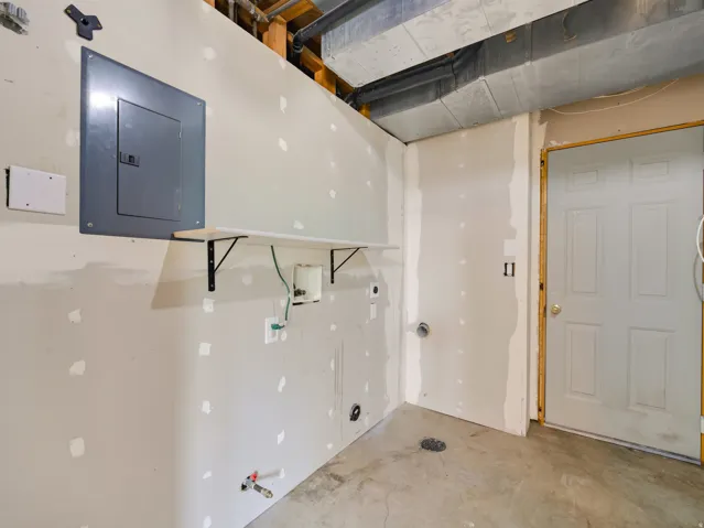 Utility area featuring drywall installation, exposed ceiling joists, concrete flooring, and a white paneled door