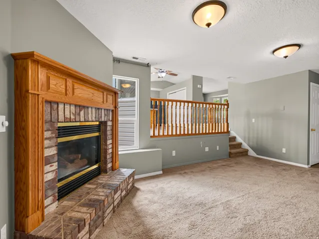 Brick fireplace with a wood-finish mantel and hearth, set within a carpeted room featuring a wood-finish baluster railing and staircase