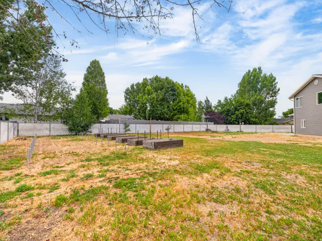 Expansive backyard featuring multiple raised garden beds, a partial privacy fence, and mature perimeter trees