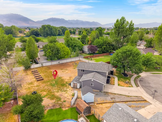 Aerial perspective of a property featuring a gray two-story residence with a dark gray shingled roof, a light blue detached shed, and a smaller brown shed