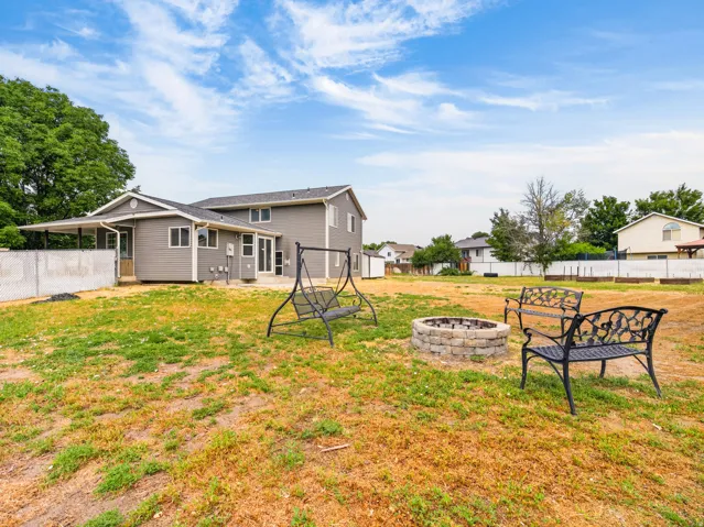 Expansive backyard featuring a stone fire pit, covered patio, and a two-story residence with gray siding