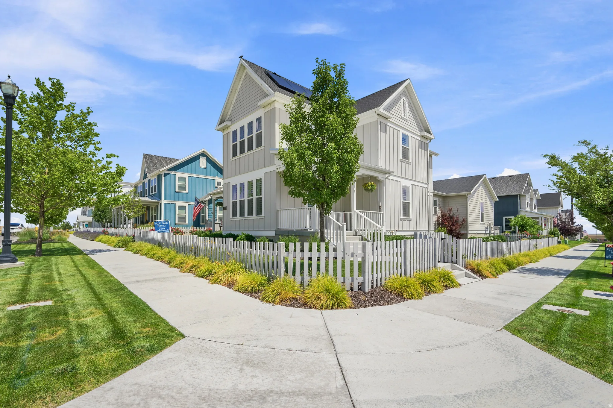 Two-story residence featuring light gray vertical siding, a front porch with white railings, and a white picket fence