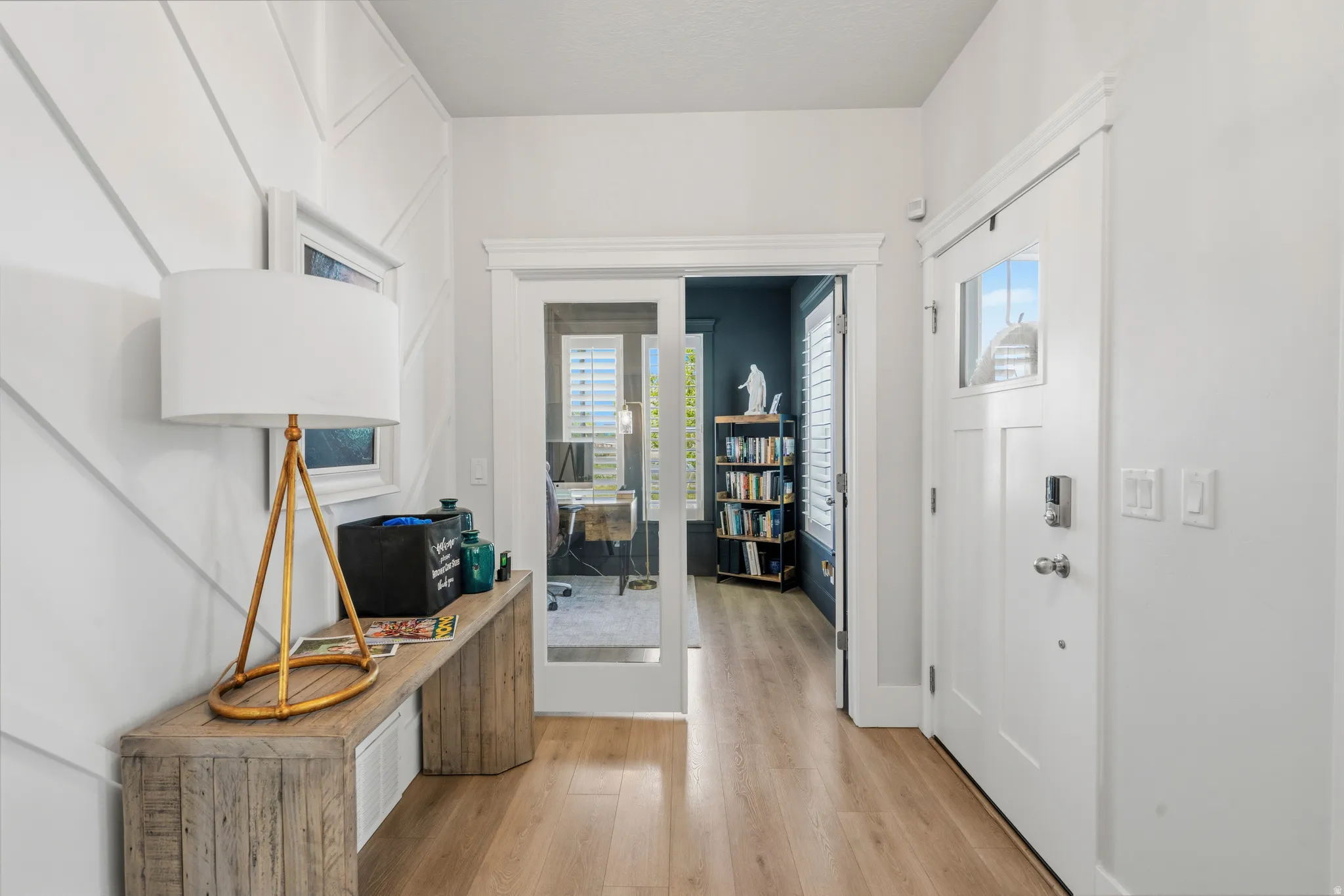 Entryway featuring chevron accent wall paneling, light wood-finish flooring, and a solid core entry door with frosted glass detailing