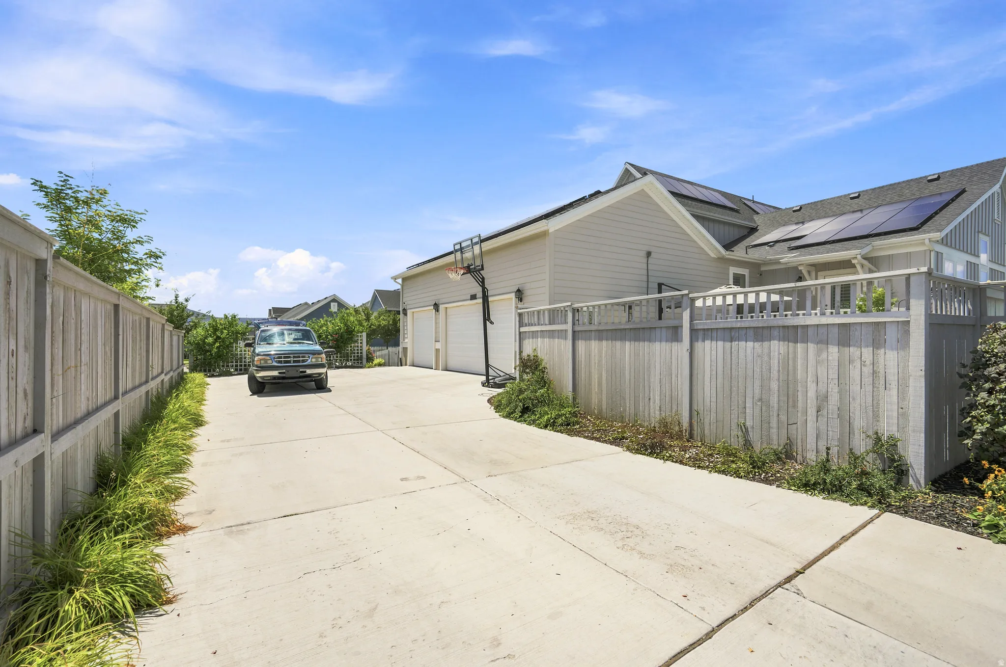 Extensive concrete driveway with perimeter fencing and mature landscaping, leading to a two-car garage with white paneled doors