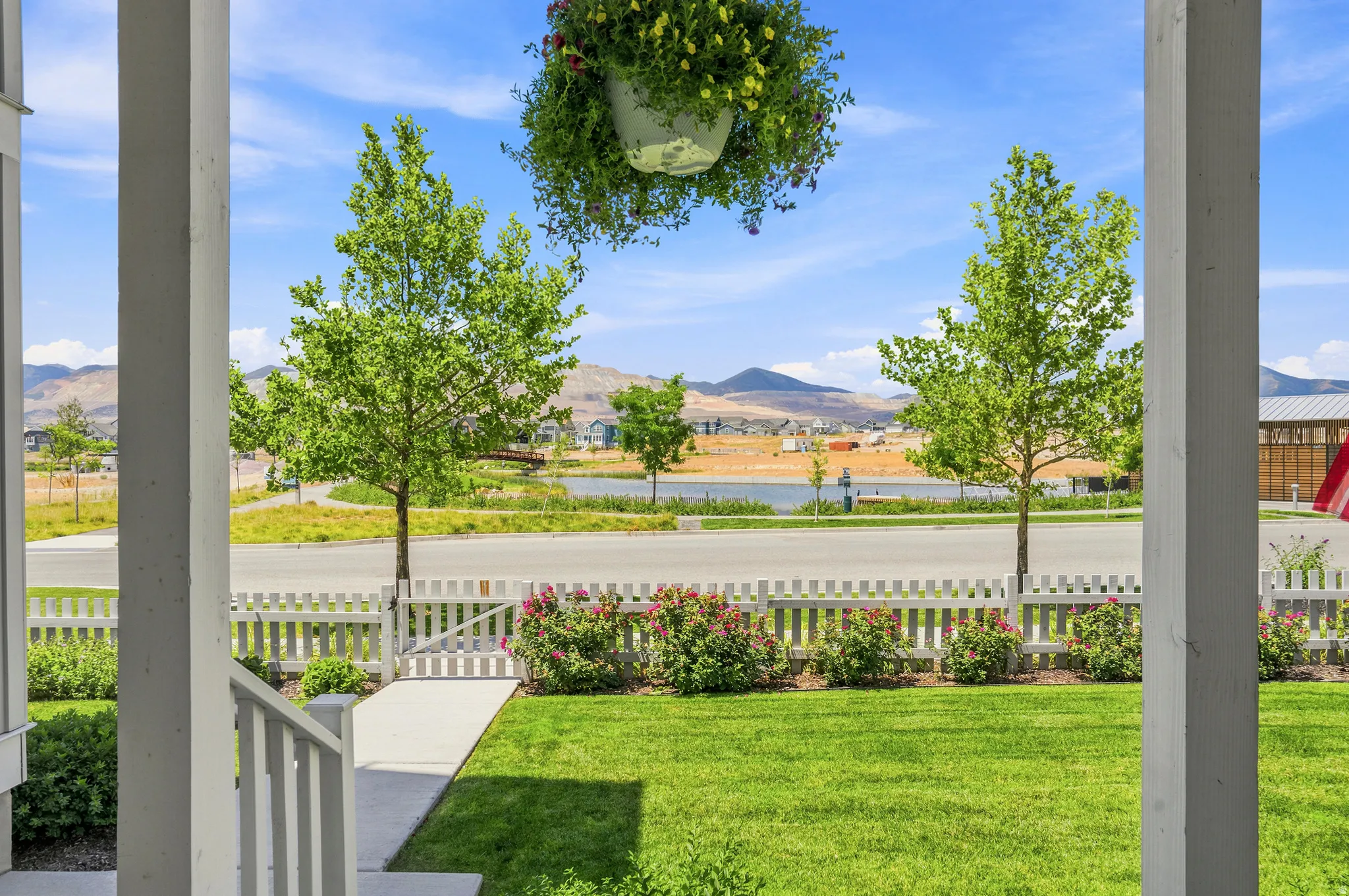 Front porch framing a manicured lawn with a white picket fence, a concrete walkway, and established landscaping