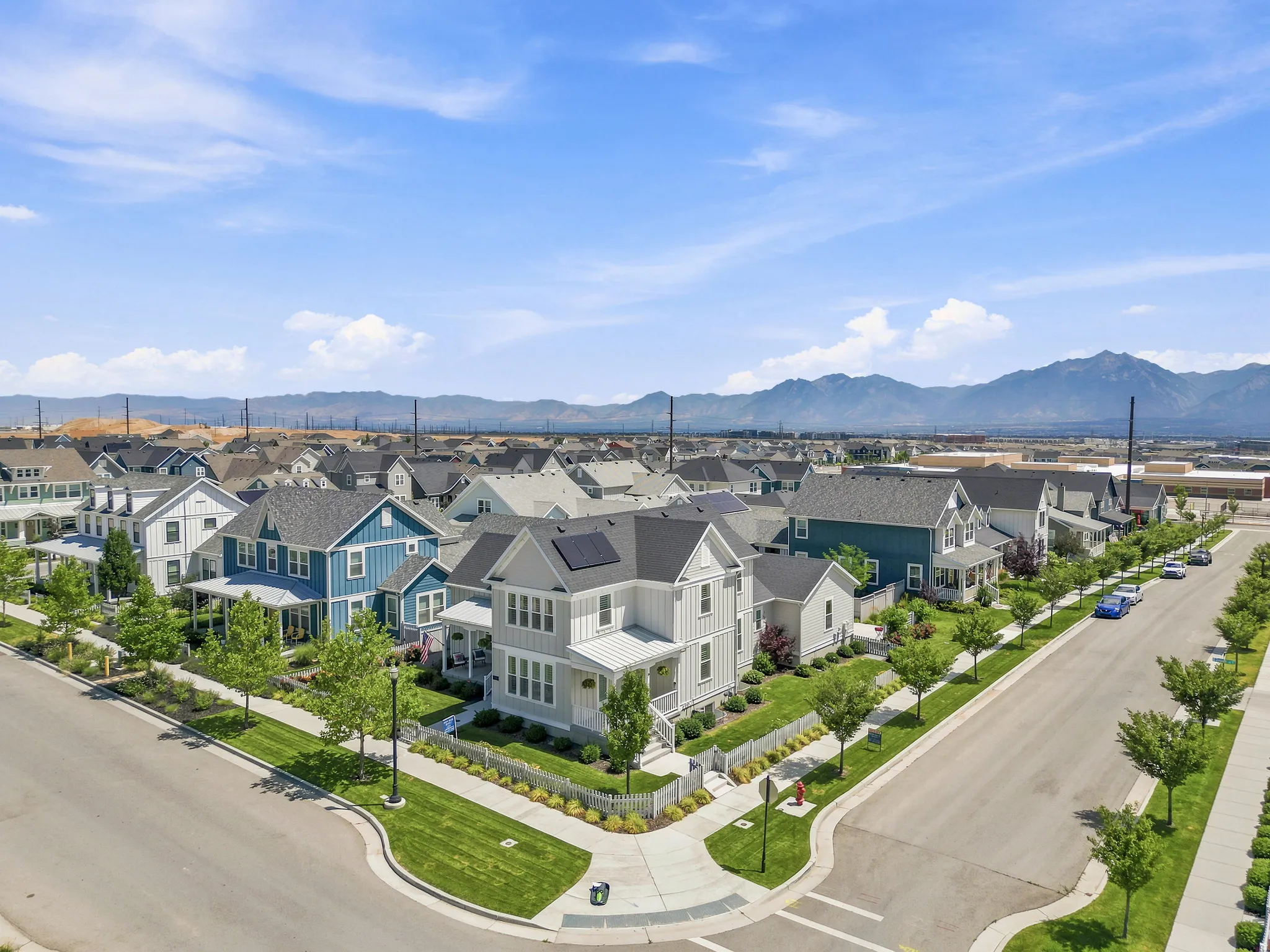 Modern residential neighborhood featuring a mix of architectural styles, tree-lined streets, sidewalks, and mountain scenery in the distance