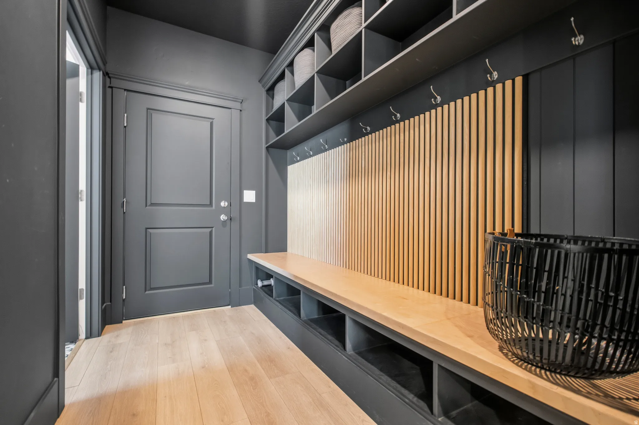 Mudroom with wood-finish flooring, built-in bench seating, storage cubbies, wall hooks, and upper shelving units