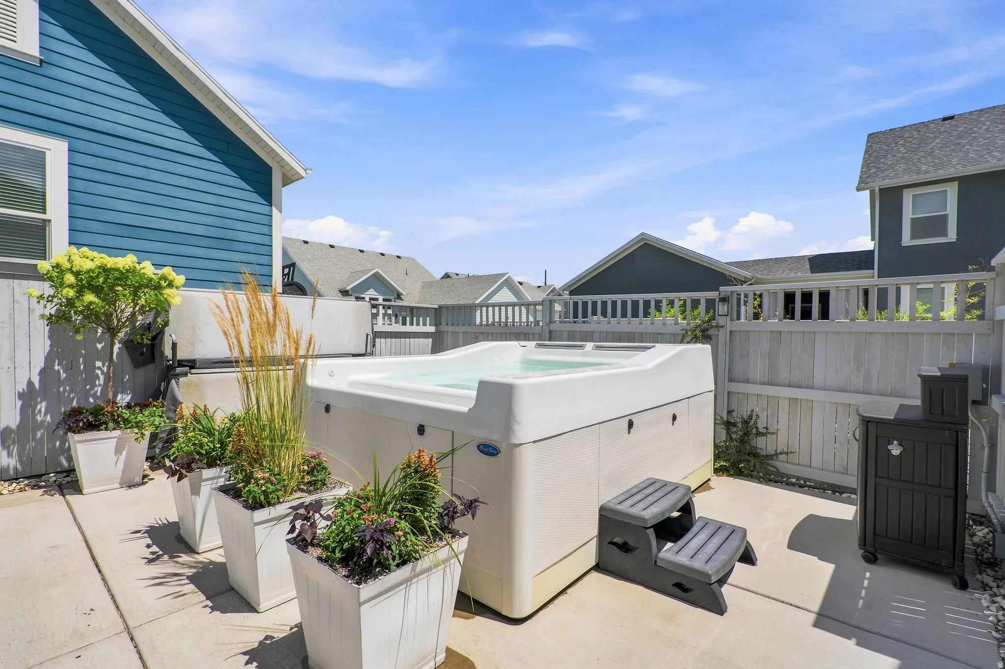 Outdoor patio featuring a hot tub with steps, multiple potted plants, and concrete paving