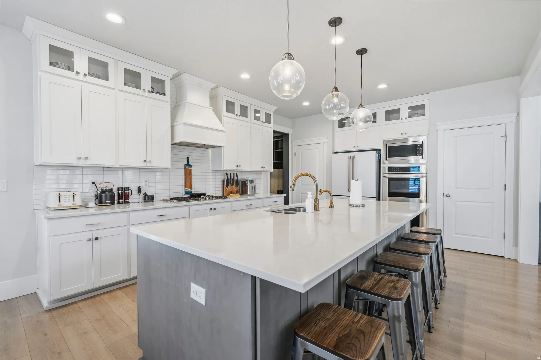 Spacious kitchen featuring an expansive central island with counter seating, white shaker cabinetry, stainless steel appliances, a subway tile backsplash, and light wood-finish flooring