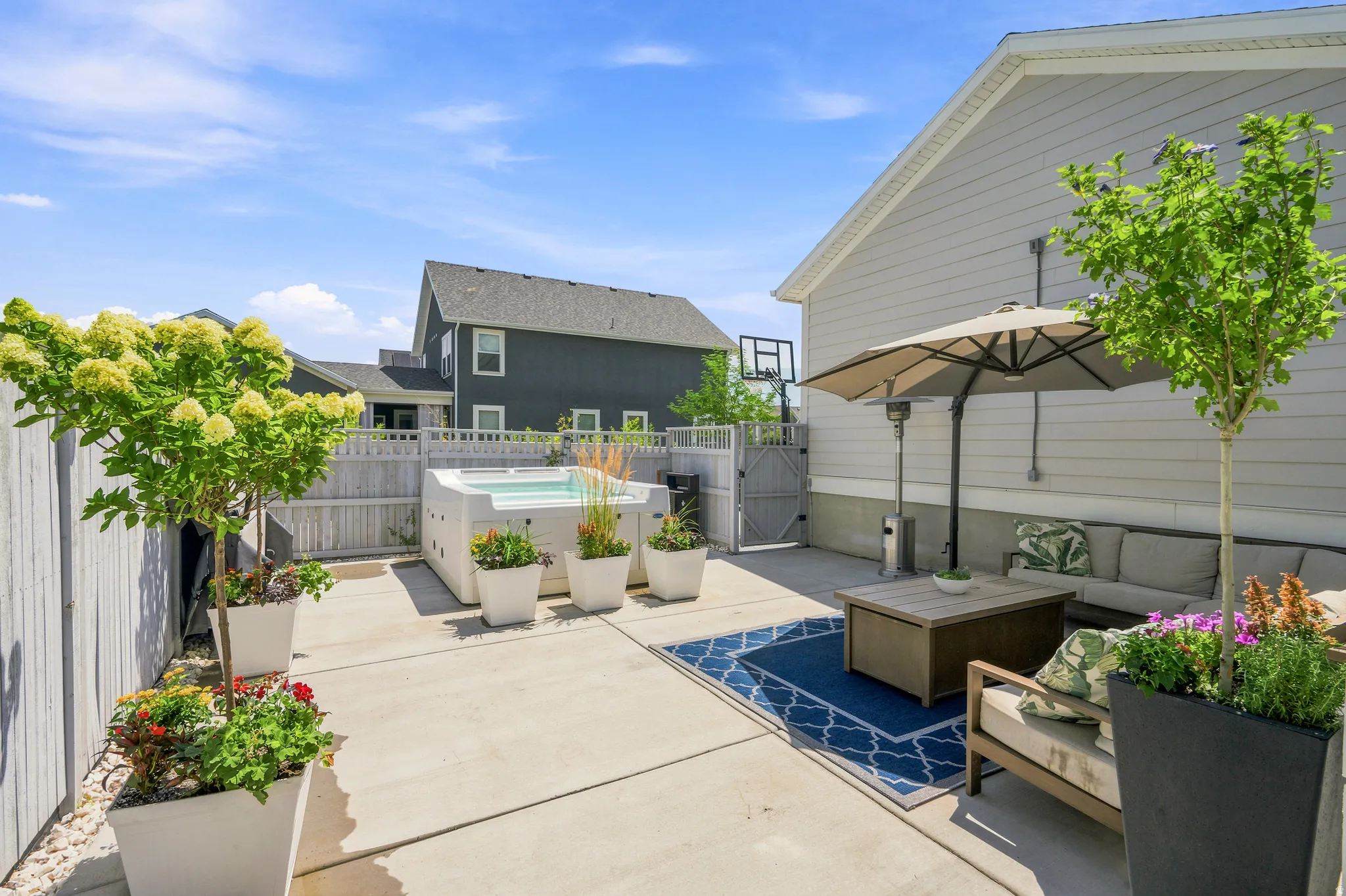 Paved patio featuring a built-in hot tub, privacy fencing, side yard gate, and mature potted landscaping