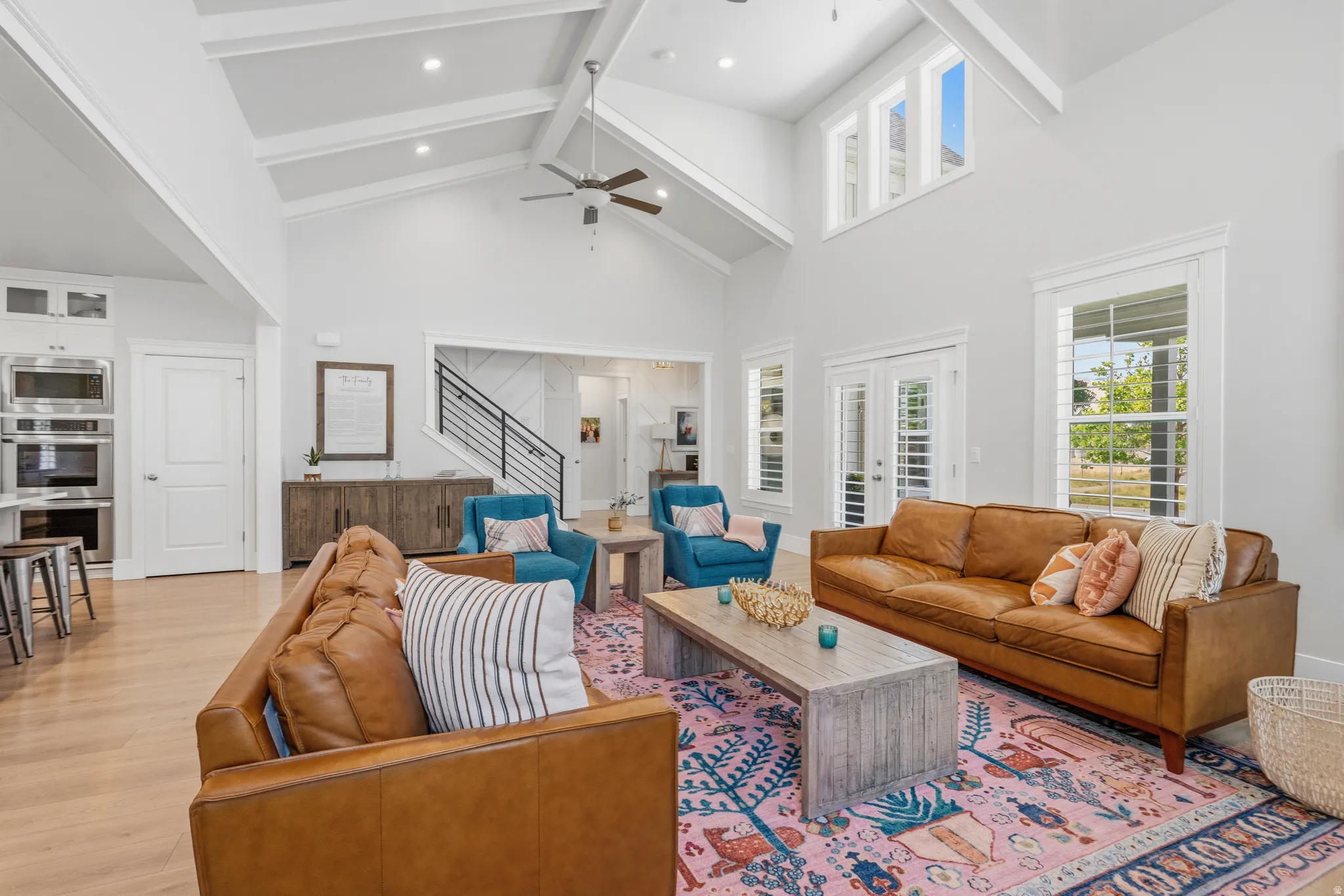 Vaulted ceilings with exposed beams, wood-finish flooring, and a contemporary ceiling fan
