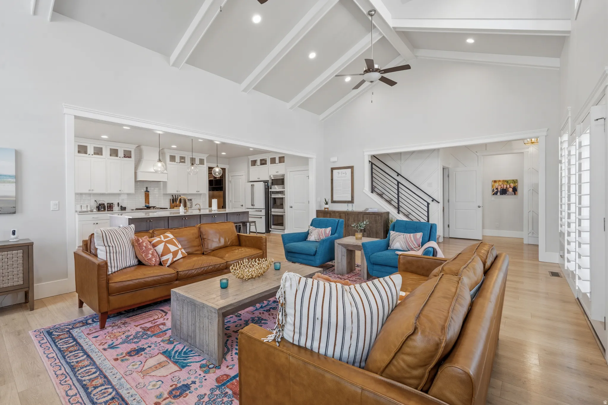 Open-concept living space featuring vaulted ceilings with exposed beams, light wood-finish flooring, and white plantation shutters