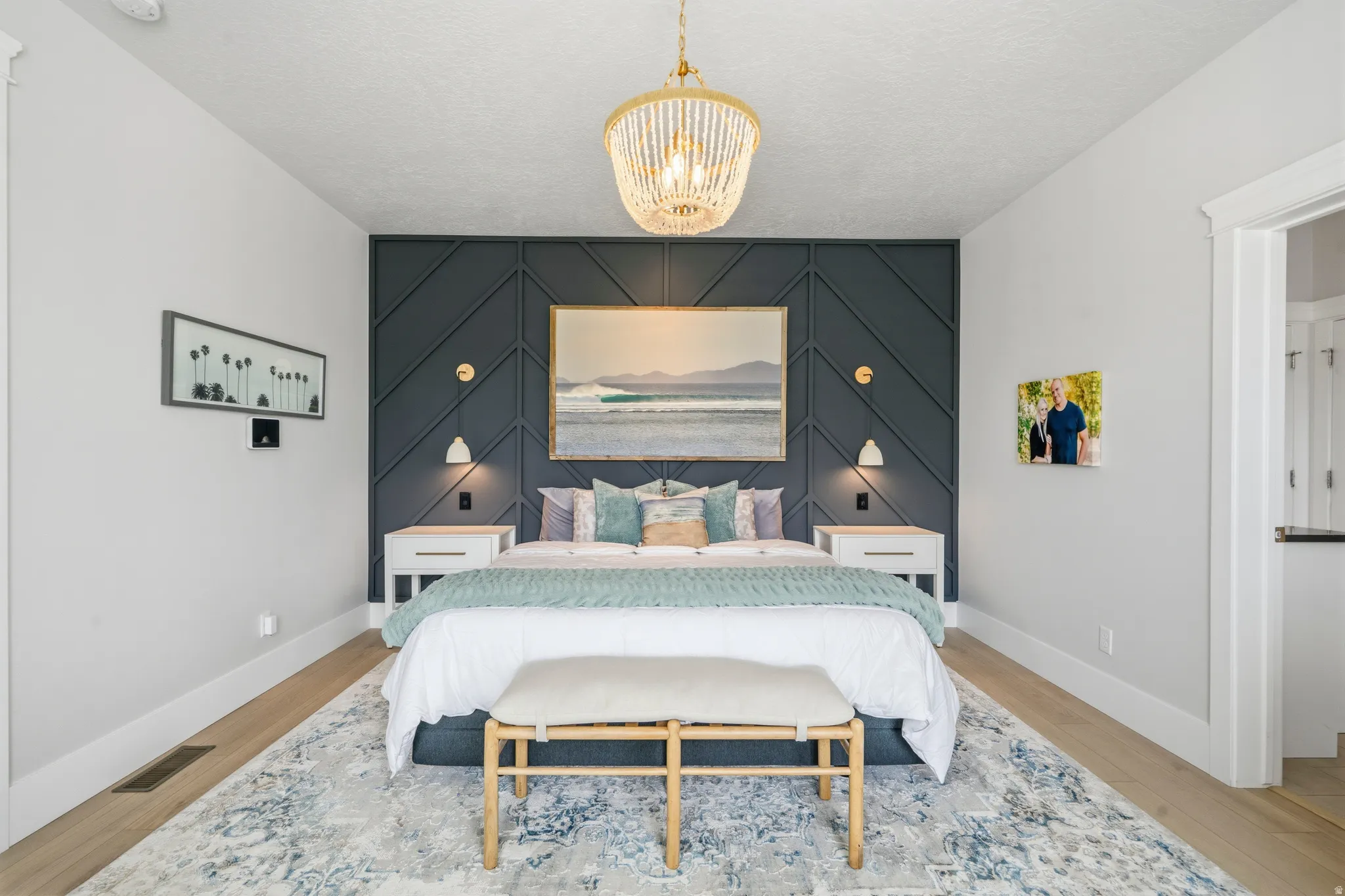Bedroom featuring a decorative accent wall with geometric paneling, light wood-finish flooring, and a detailed overhead chandelier