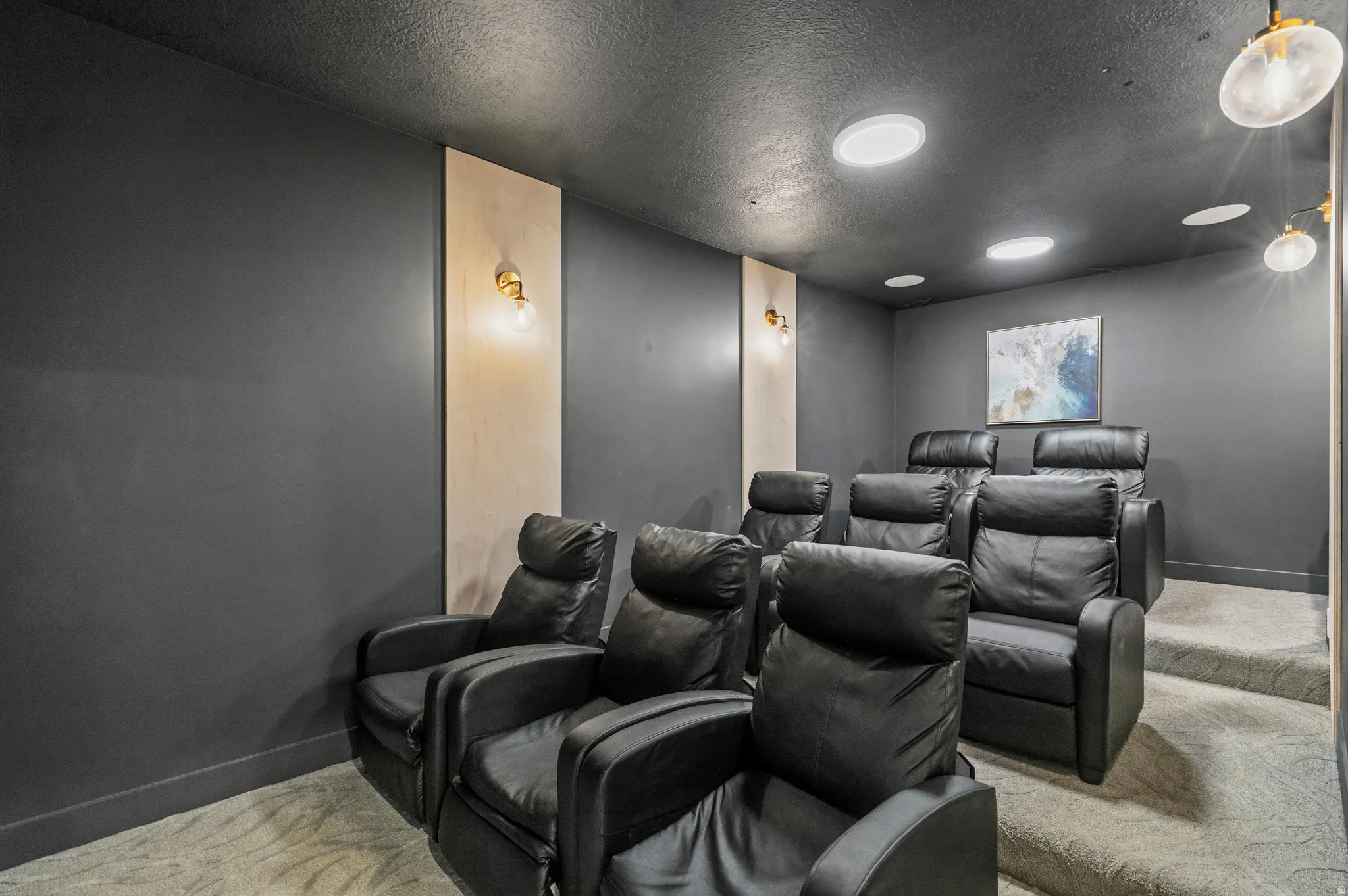 Dedicated home theater featuring tiered seating, recessed ceiling lighting, wall-mounted sconces, and plush carpet flooring