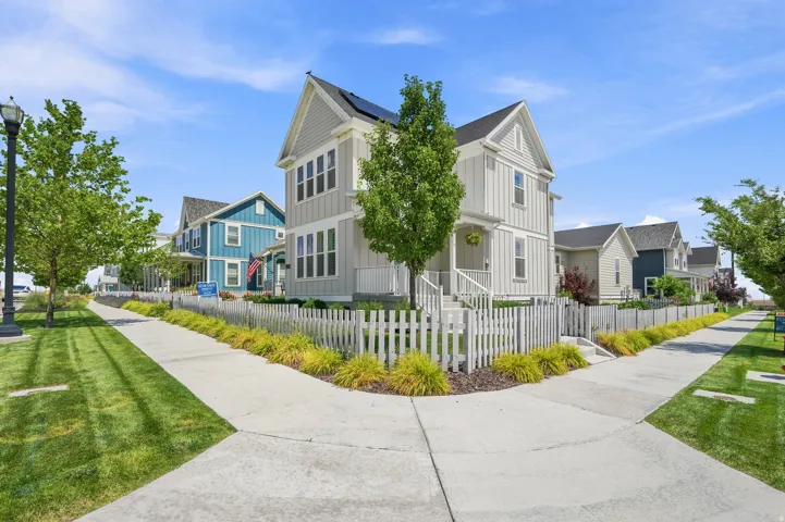 Two-story residence featuring light gray vertical siding, a front porch with white railings, and a white picket fence
