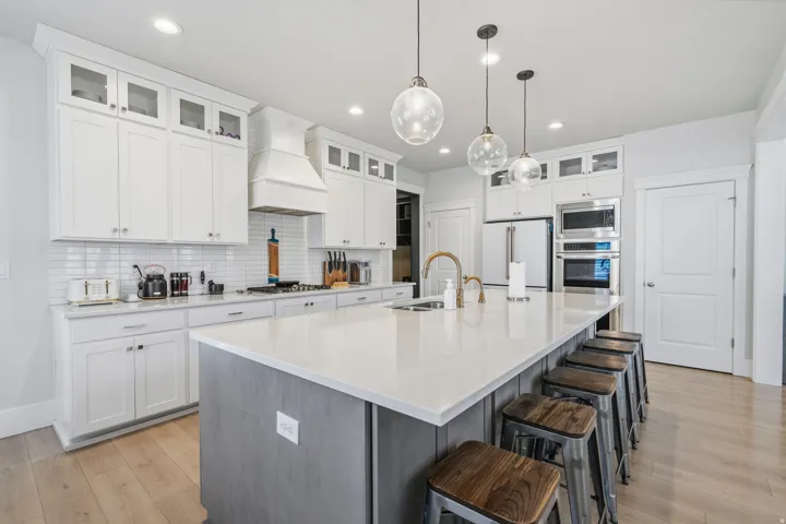 Spacious kitchen featuring an expansive central island with counter seating, white shaker cabinetry, stainless steel appliances, a subway tile backsplash, and light wood-finish flooring