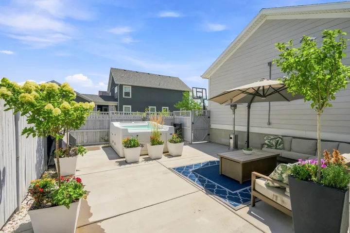 Paved patio featuring a built-in hot tub, privacy fencing, side yard gate, and mature potted landscaping