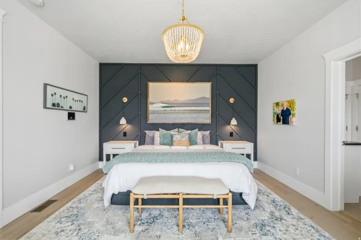 Bedroom featuring a decorative accent wall with geometric paneling, light wood-finish flooring, and a detailed overhead chandelier