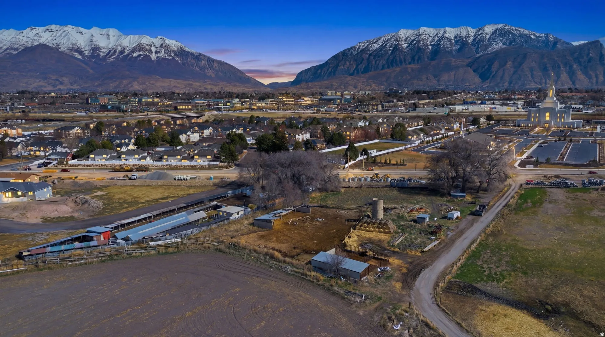 Expansive property featuring agricultural structures, open fields, and a winding dirt road