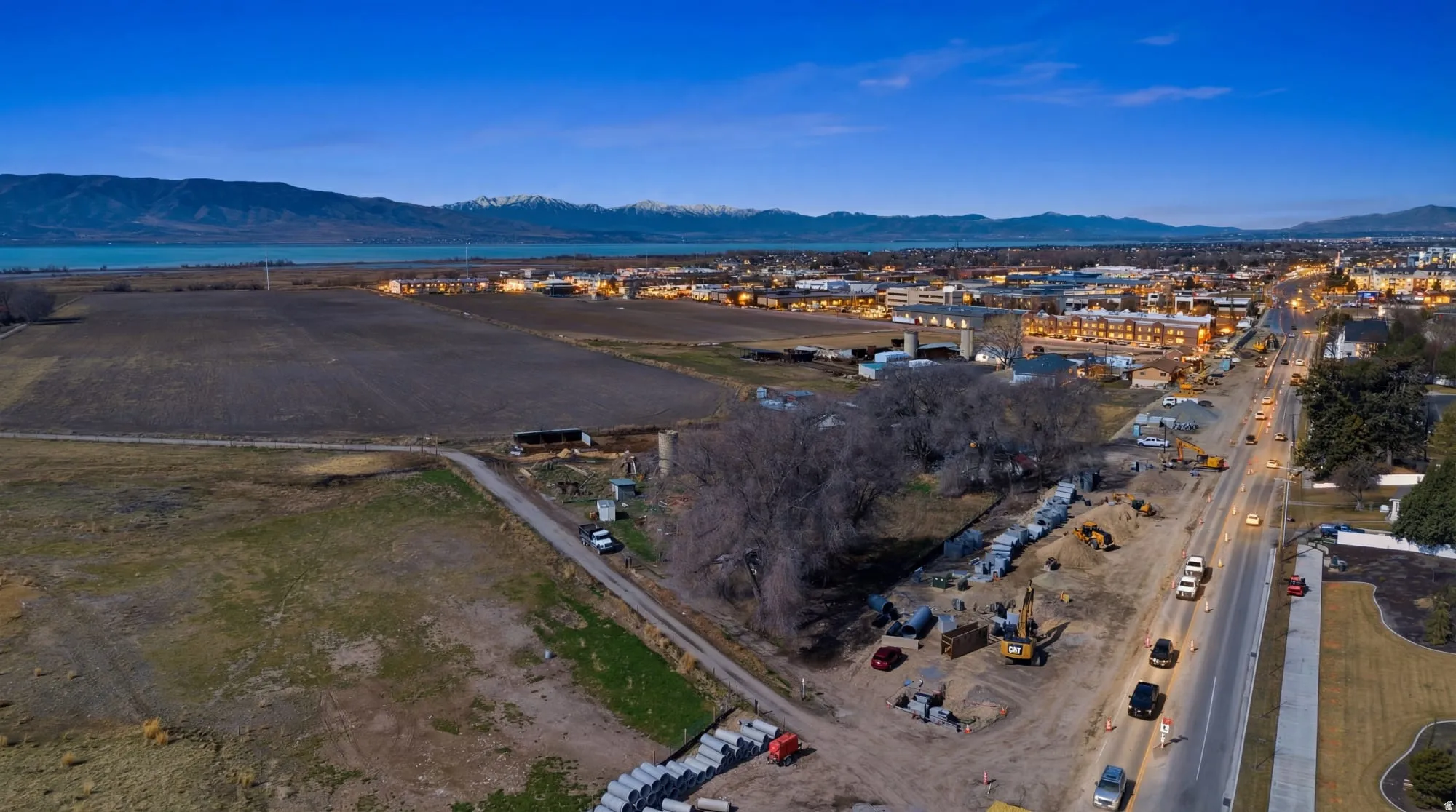 Aerial perspective showcasing a large agricultural field, a body of water, and distant snow-capped mountains