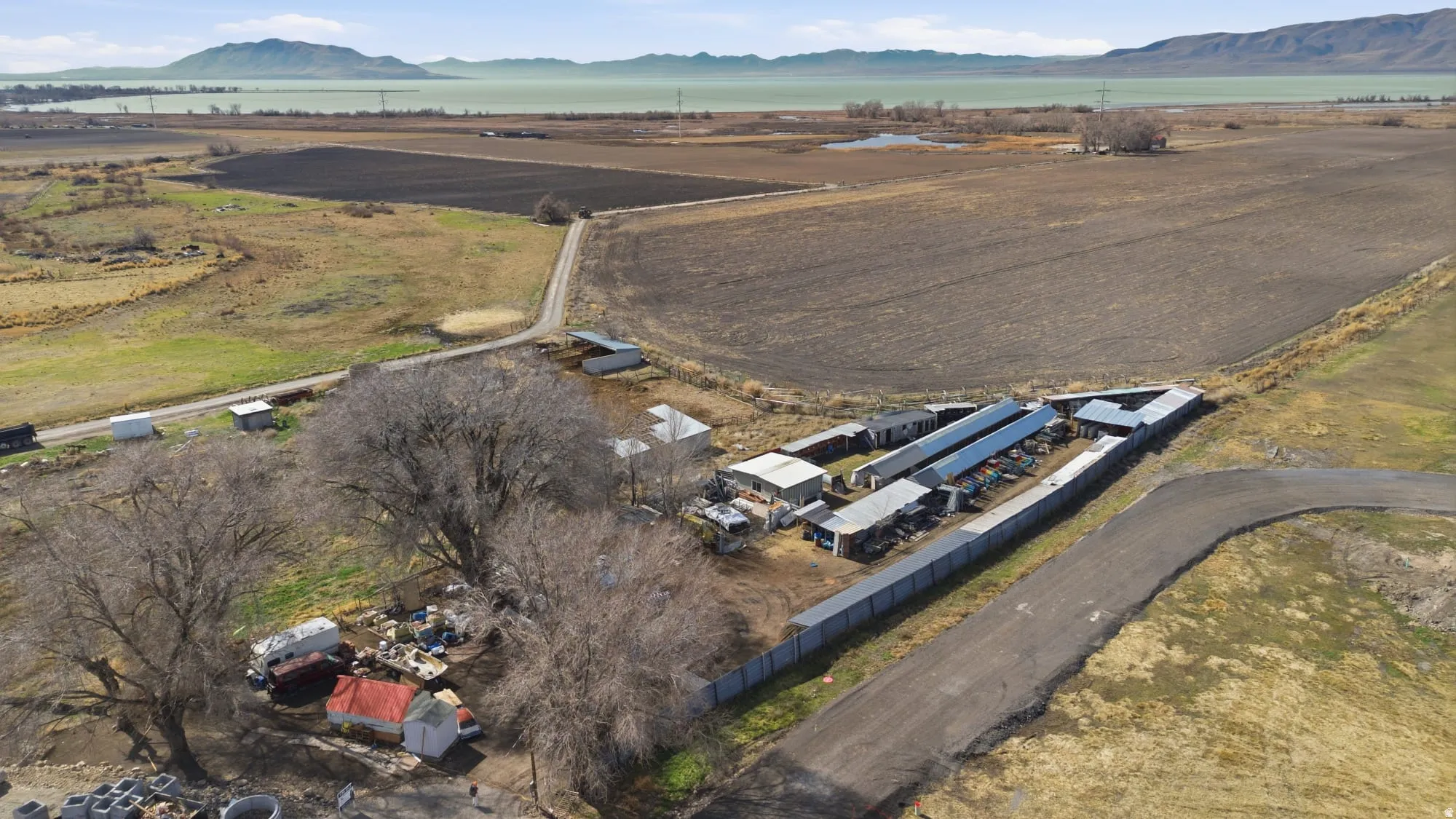 Expansive rural property featuring multiple outbuildings, agricultural fields, and a distant body of water with mountainous backdrop