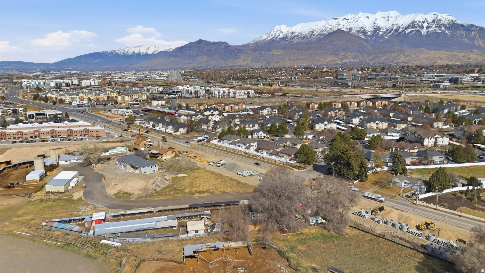 Expansive property featuring multiple outbuildings, agricultural fields, and a paved road frontage, with mountain scenery in the background
