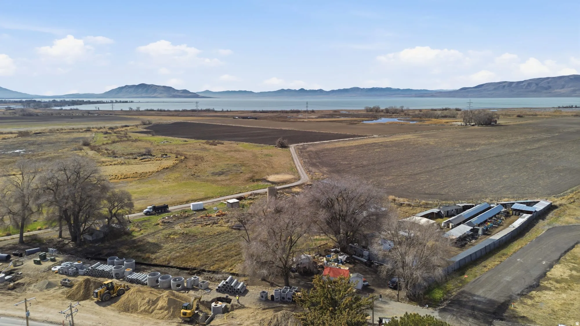 Expansive land parcel featuring agricultural fields, mature trees, and a distant lake