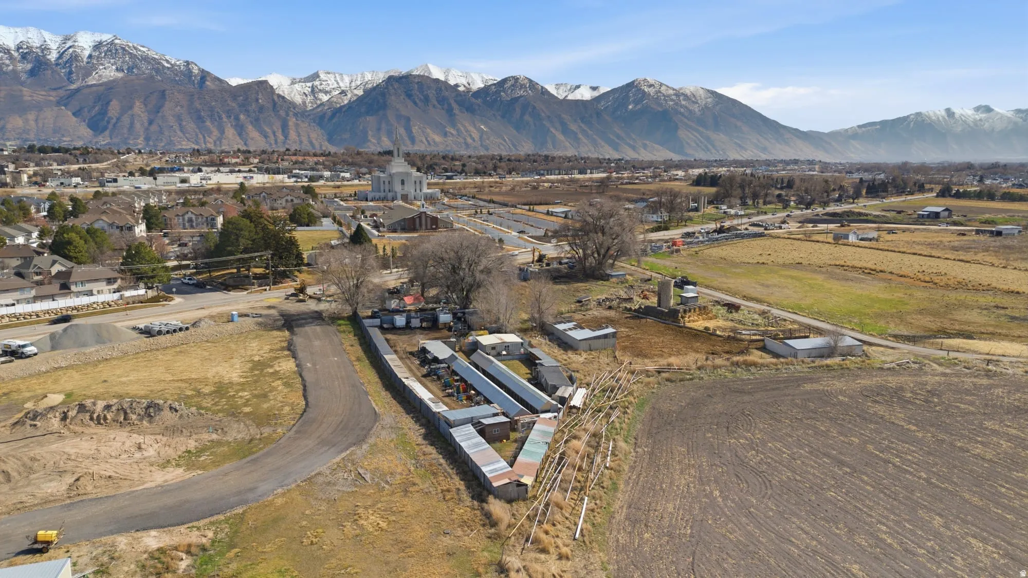 Expansive undeveloped land featuring a cleared building site, mature trees, and existing outbuildings