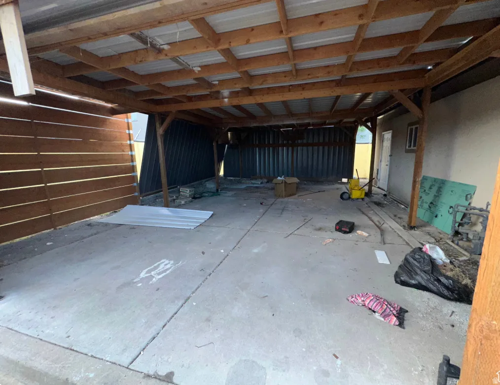 Covered outdoor structure featuring a concrete slab foundation, exposed wood beam ceiling, metal roof, and slatted wood wall