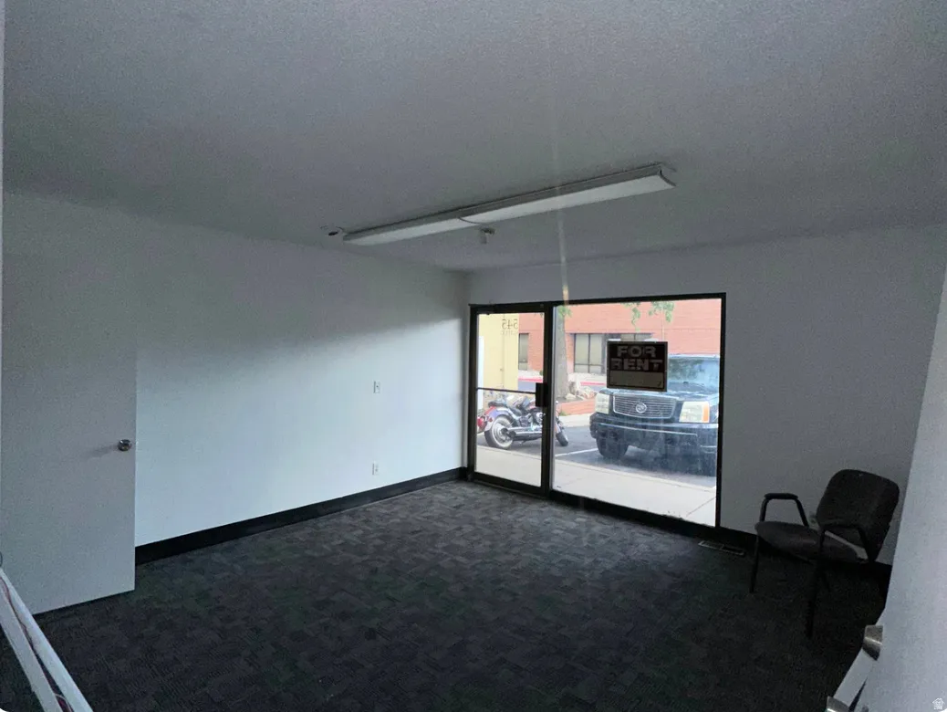 Commercial space featuring dark patterned carpet flooring, white painted walls, and a dark baseboard trim