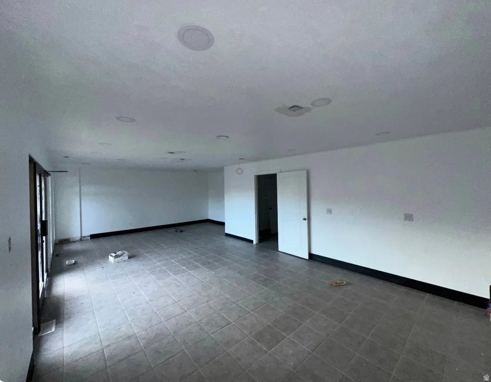 Spacious interior featuring grey tile flooring, white walls, multiple recessed ceiling lights, and a white interior door