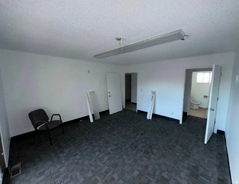 Spacious room featuring patterned carpet flooring, white painted walls, and a fluorescent ceiling light fixture