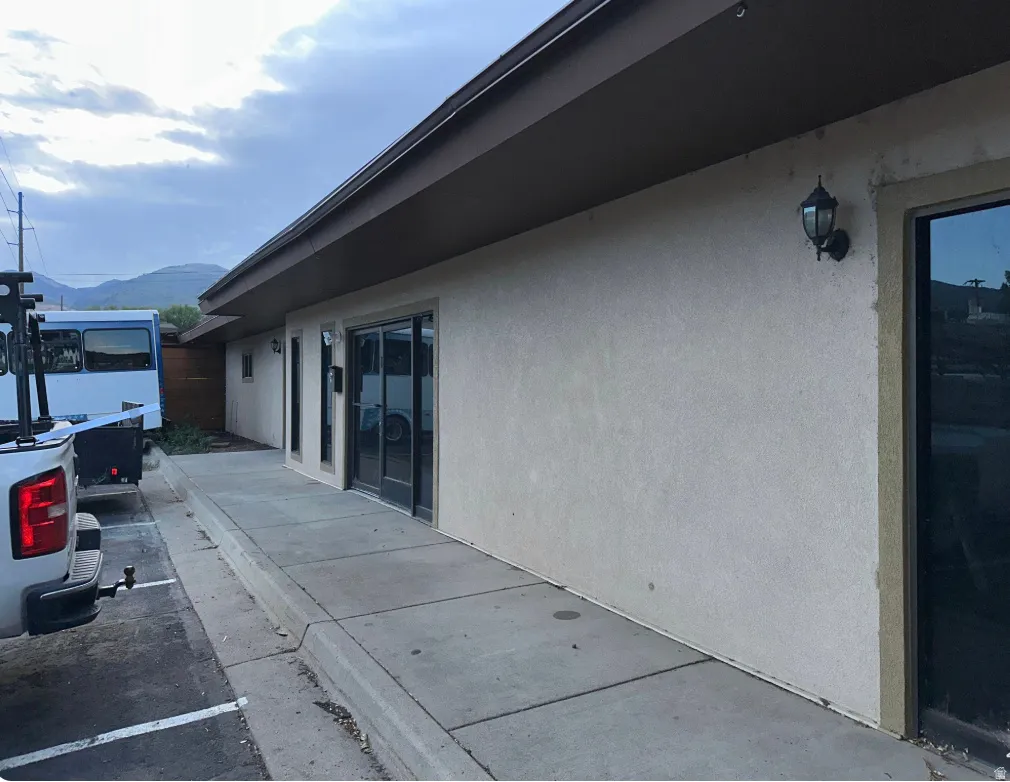 Stucco exterior with brown trim, featuring multiple exterior wall sconces, large glass sliding doors, and a concrete walkway