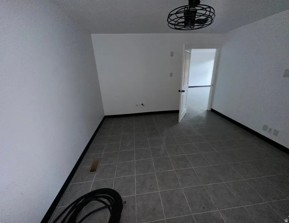 Room featuring dark gray tile flooring, white walls, and a black ceiling fan with an exposed bulb design