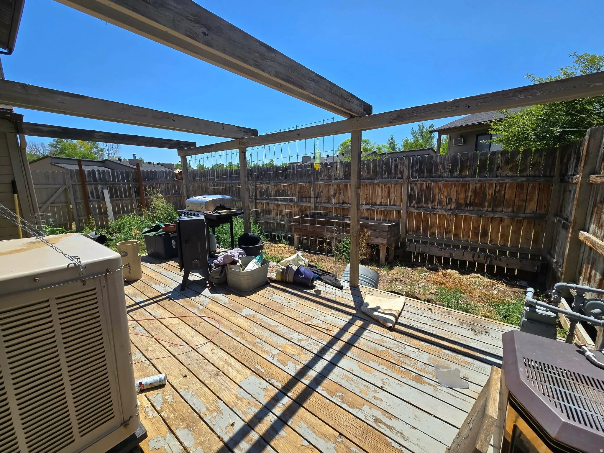 Outdoor wood-decked patio with an open pergola structure and perimeter wood fencing