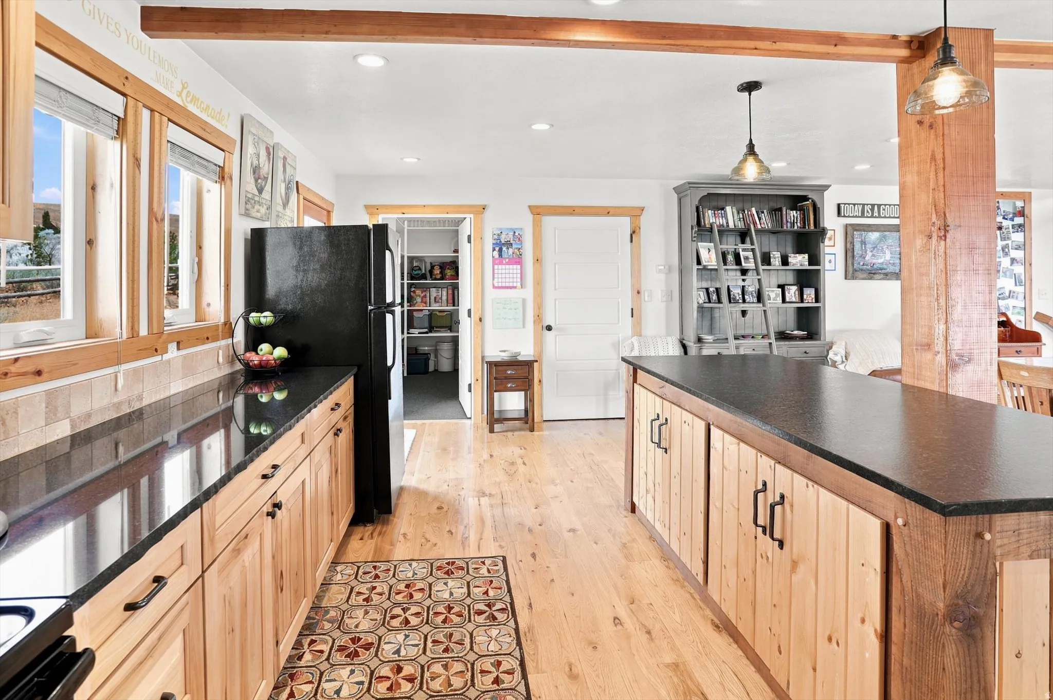 Open-concept kitchen featuring wood-finish flooring, a central island with a dark countertop, and exposed wood beams