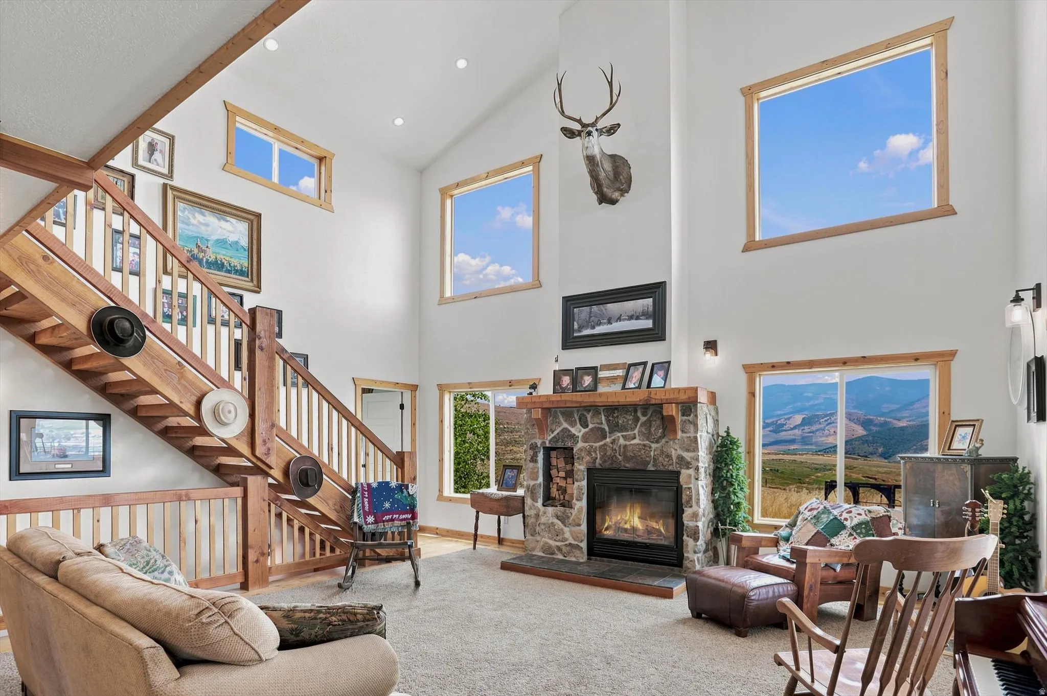 Vaulted living space featuring a stone-clad fireplace with mantel, an open-tread wood staircase, and multiple windows with wood trim