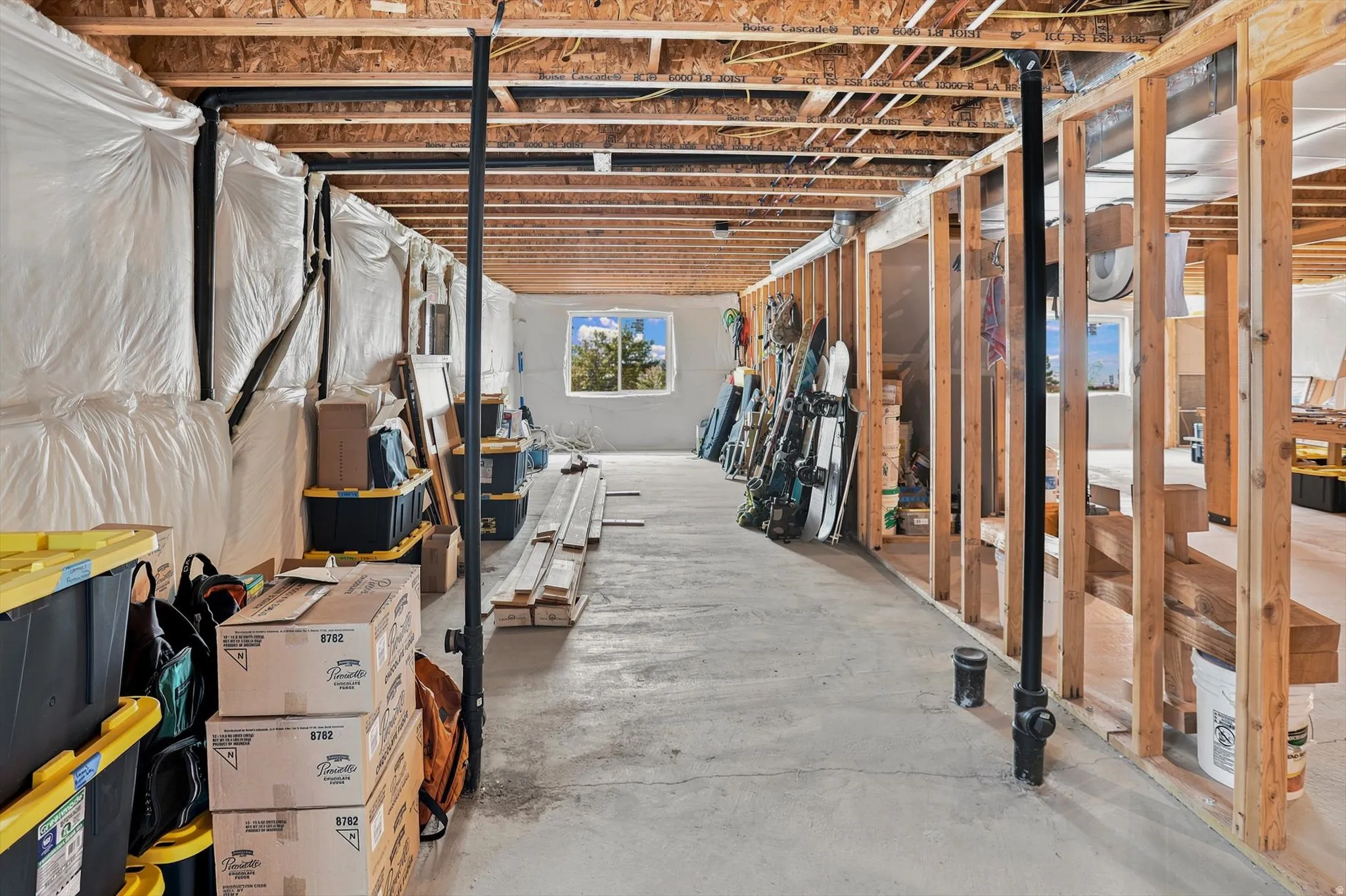 Unfinished basement providing expansive open space and structural framing, featuring a concrete floor, exposed ceiling joists, and a visible window with outdoor scenery