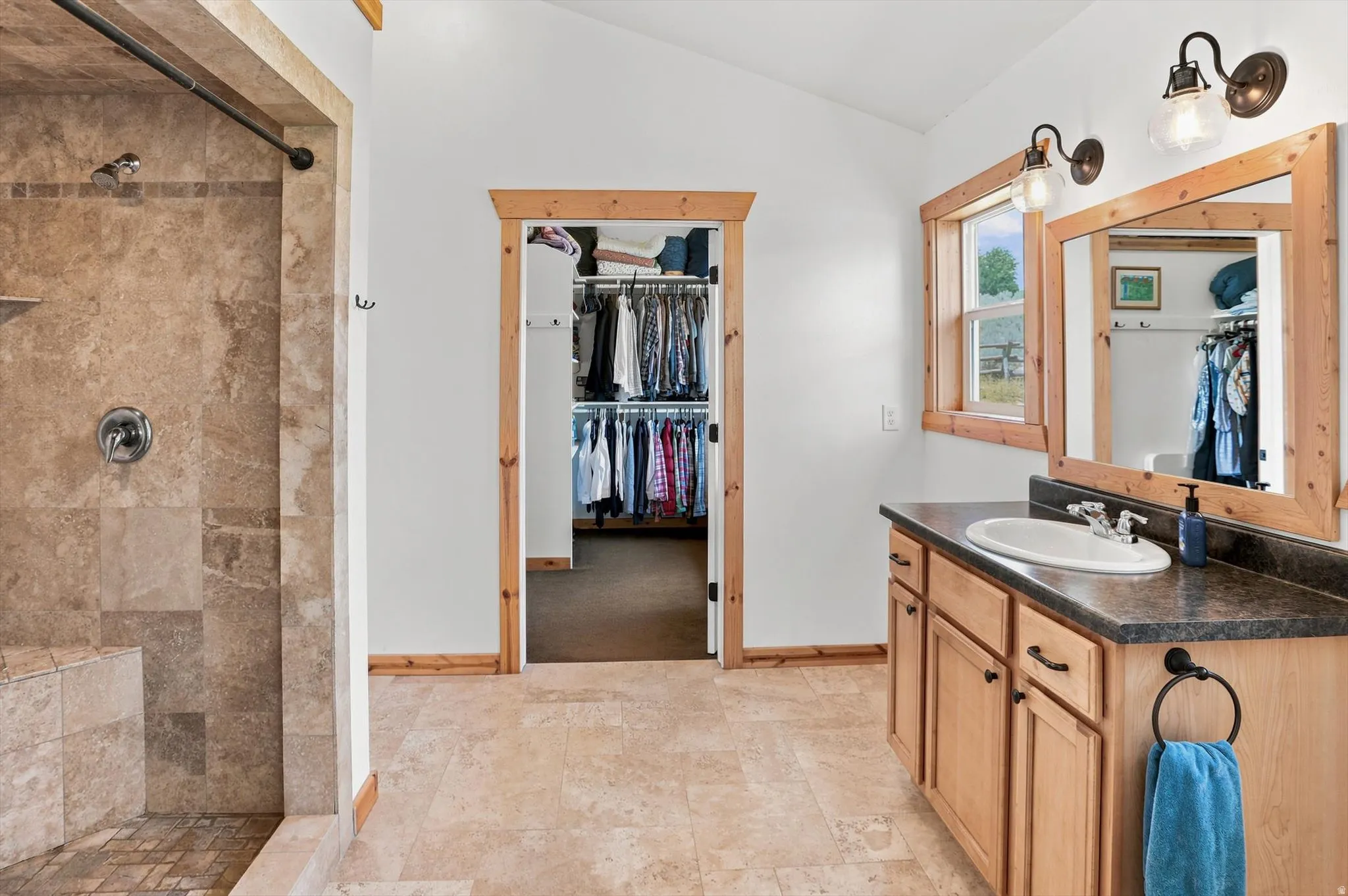 Primary Suite Bathroom featuring a walk-in shower with tile surround and integrated bench, wood-finish vanity with countertop and integrated sink, framed mirror, and wood-finish trim throughout